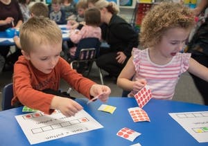 Two children working with stickers and papers at a table in a classroom
