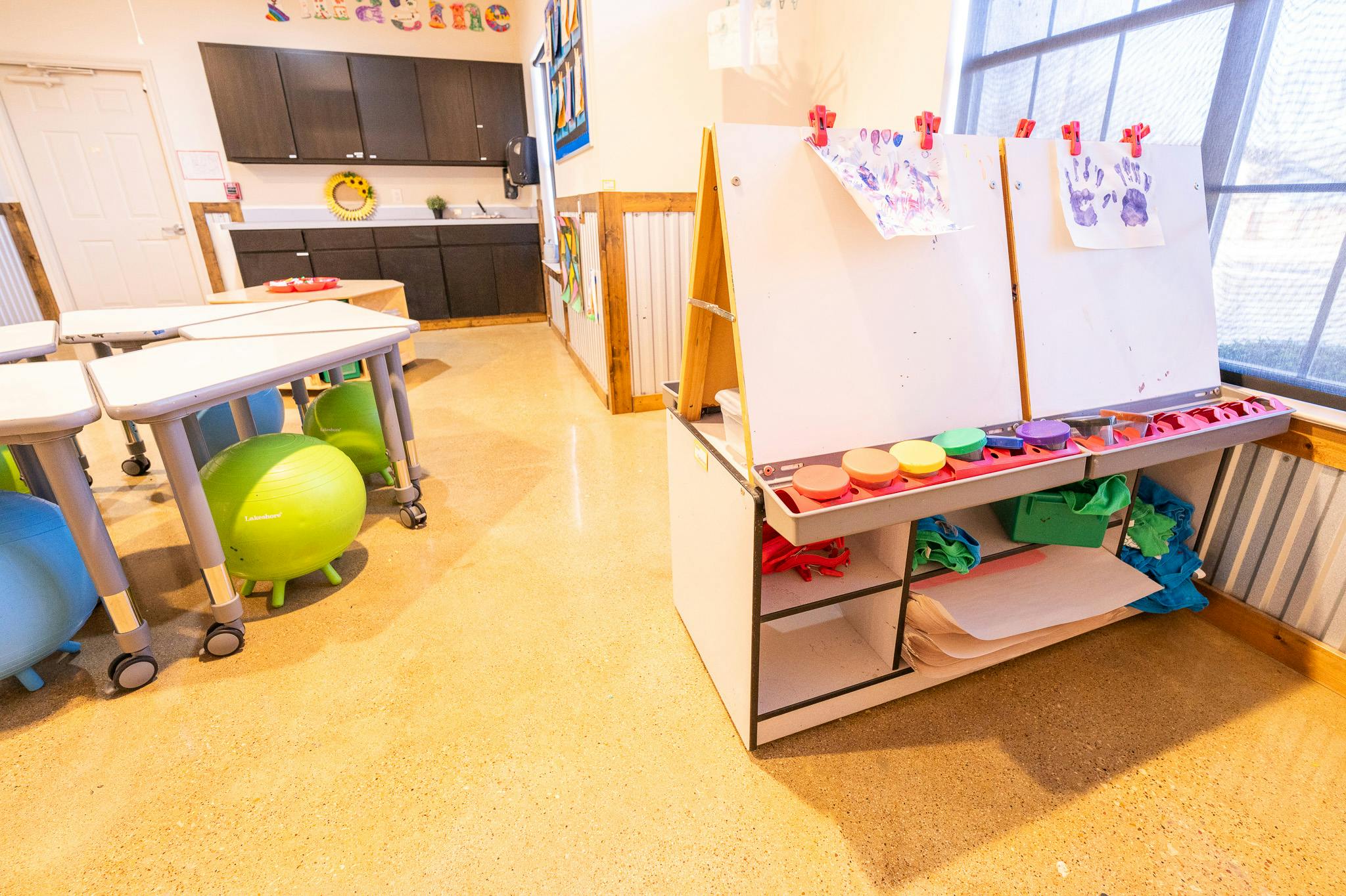 Art easel with children's artwork and paint supplies in a classroom