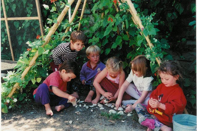 Children playing with shells under a plant-covered structure