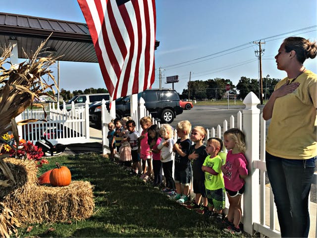 Adult and children standing with hands over hearts near a flag