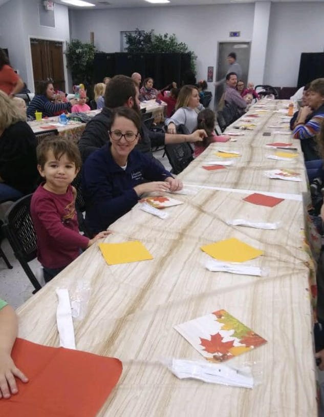 People and children sitting at a long table with autumn leaf decorations