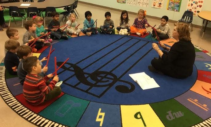 Adult and children sitting in a circle on a music-themed rug