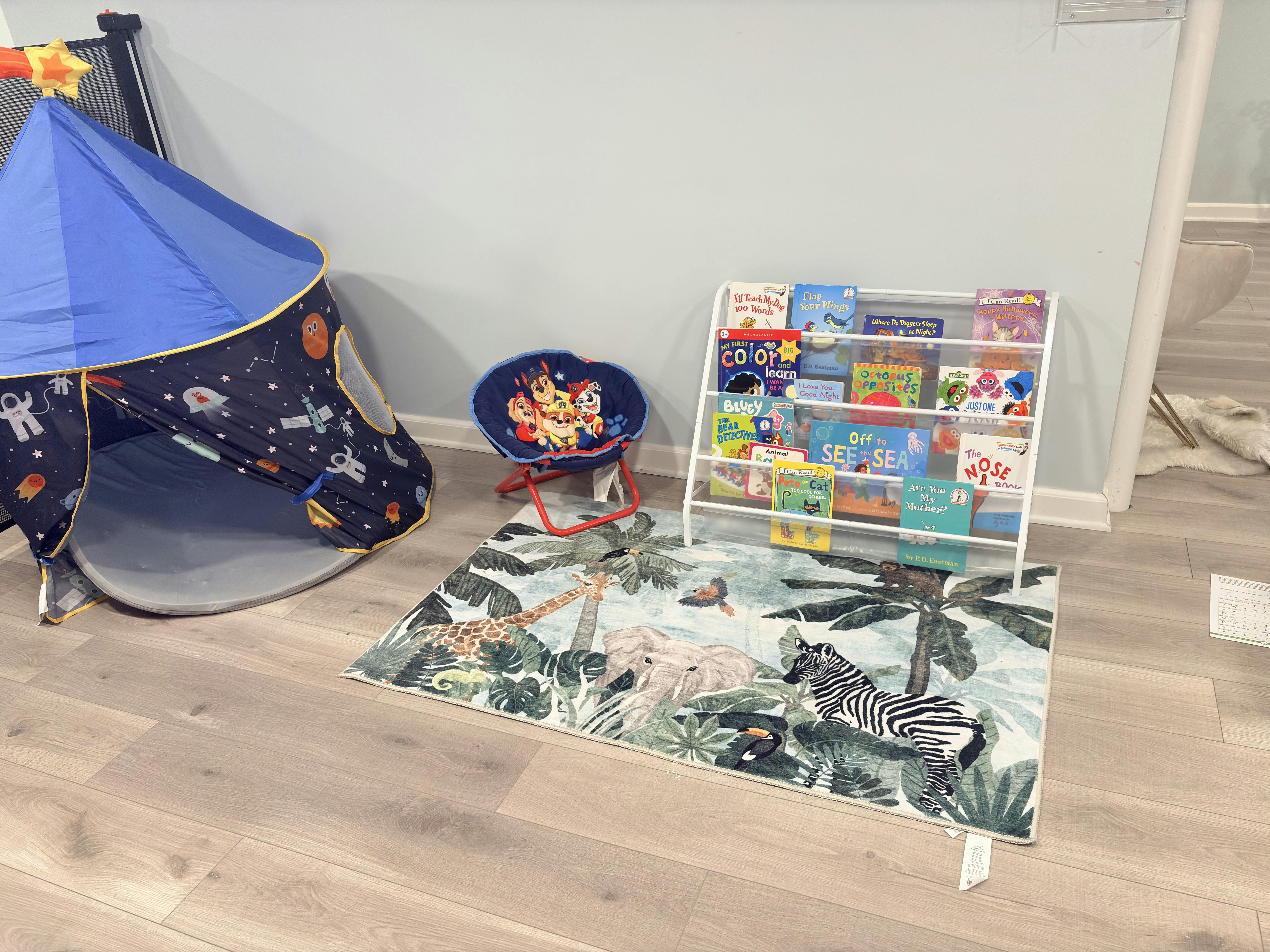 Play tent with space theme, small child's chair, book display, and animal rug