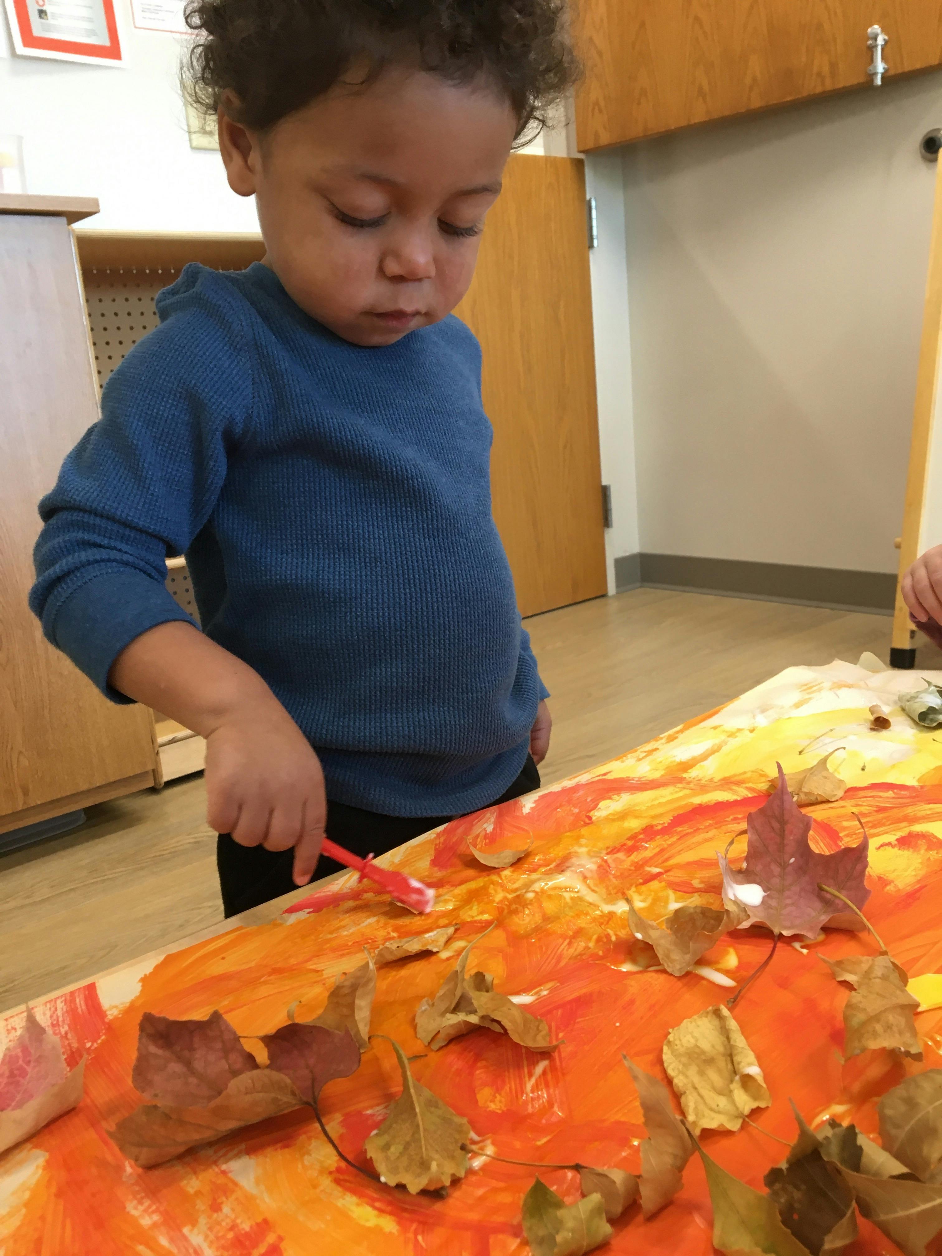 Child painting with a brush on a surface with leaves