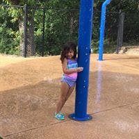 Child standing next to a blue pole at a splash pad