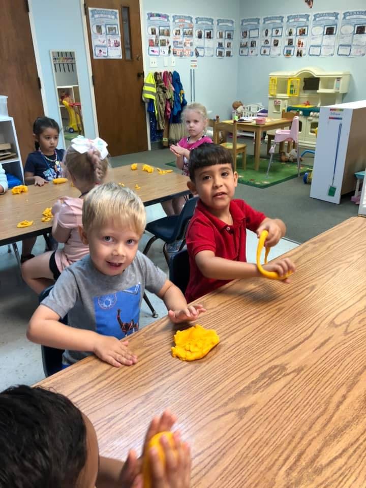 Children playing with yellow modeling clay at a table in a classroom
