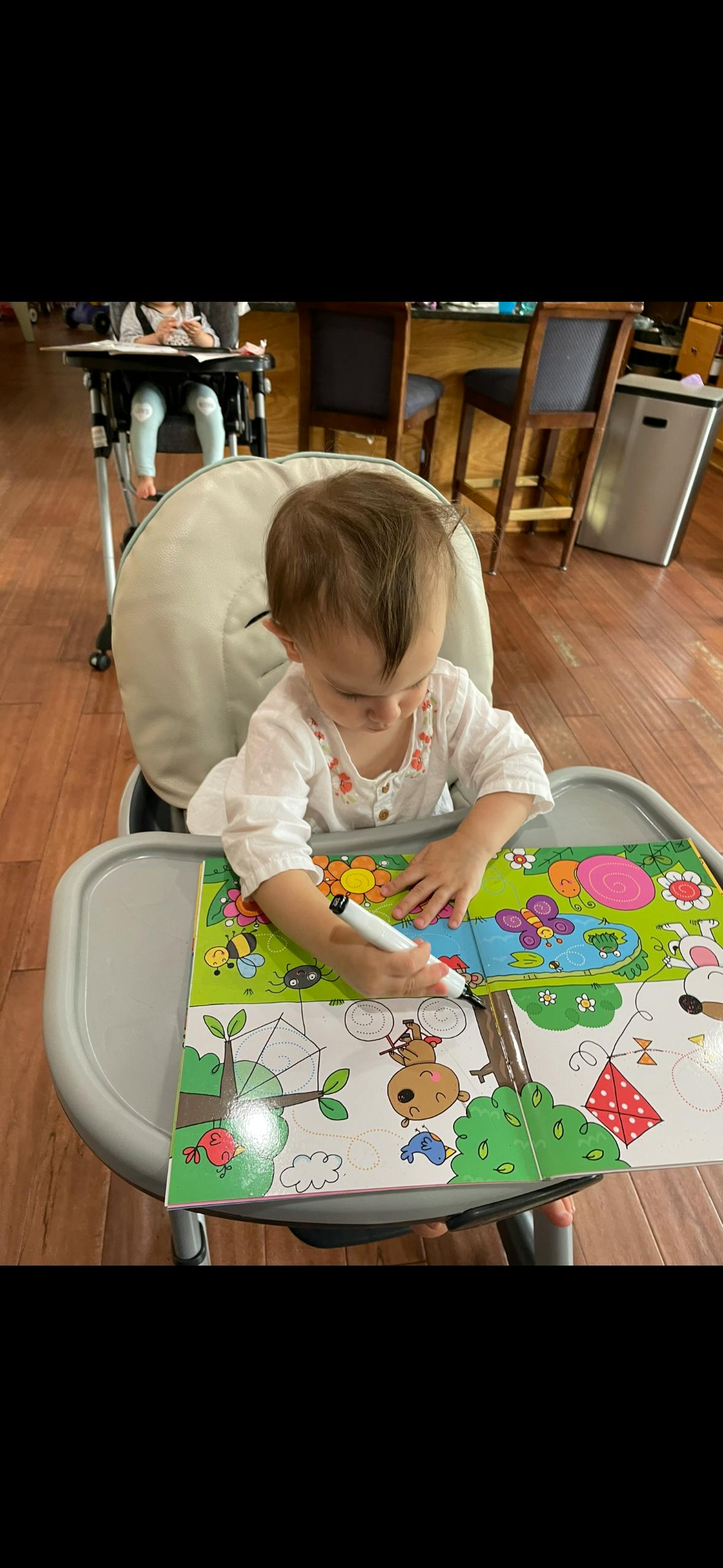 Child in a high chair drawing in a coloring book