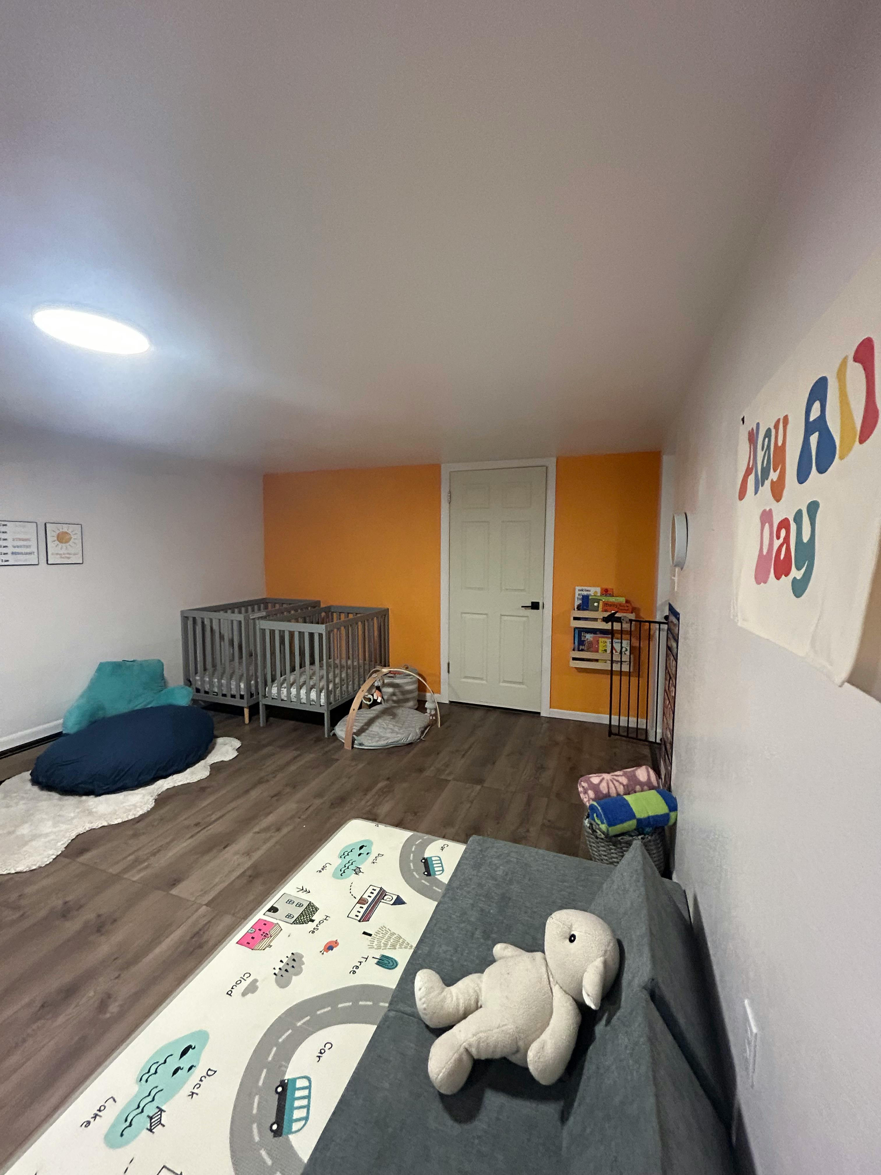 Two cribs in a room with a playmat and stuffed animal