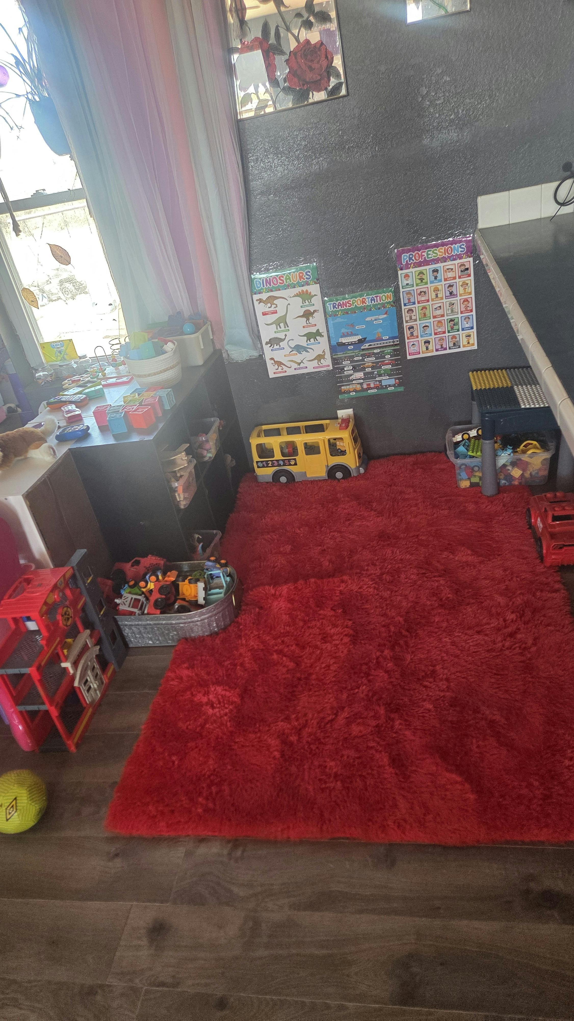 Children's play area with a red rug, toy bus, and learning posters on the wall