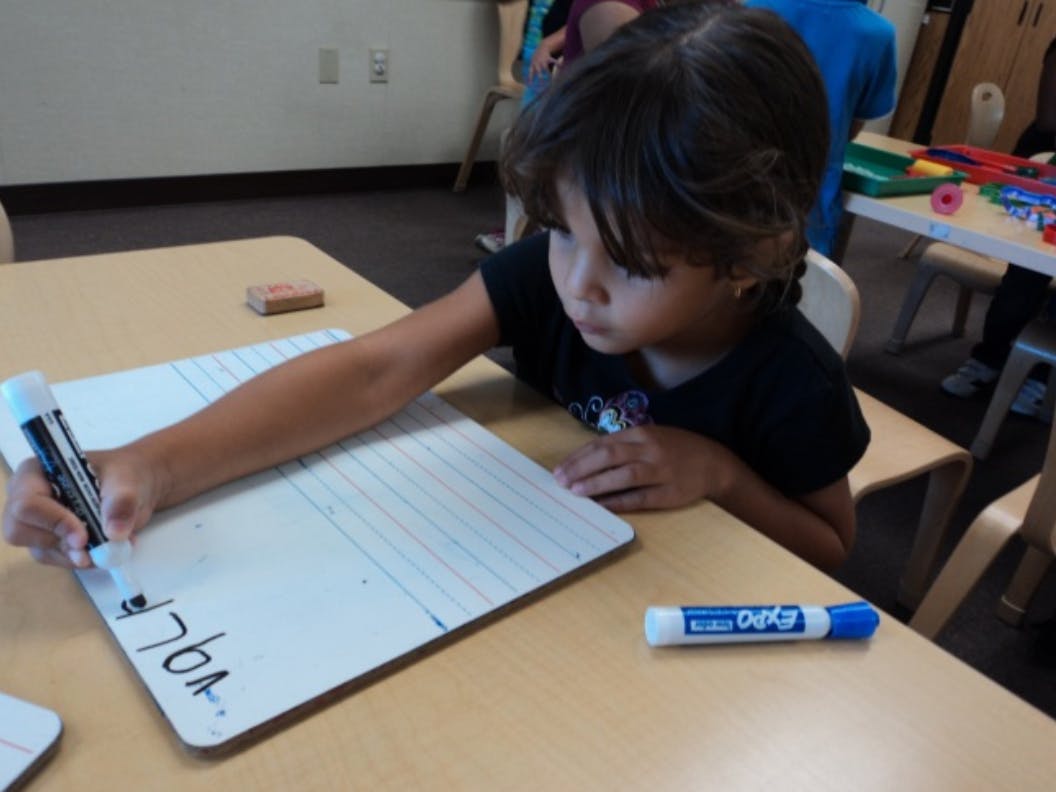 Child writing on a whiteboard with a marker