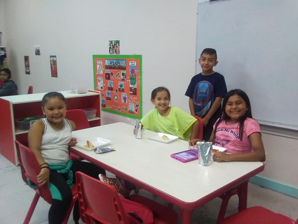 Four children sitting and standing around a table in a classroom