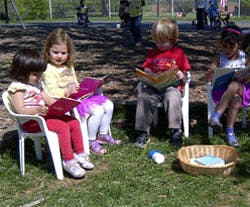 Four children sitting in chairs reading books outdoors