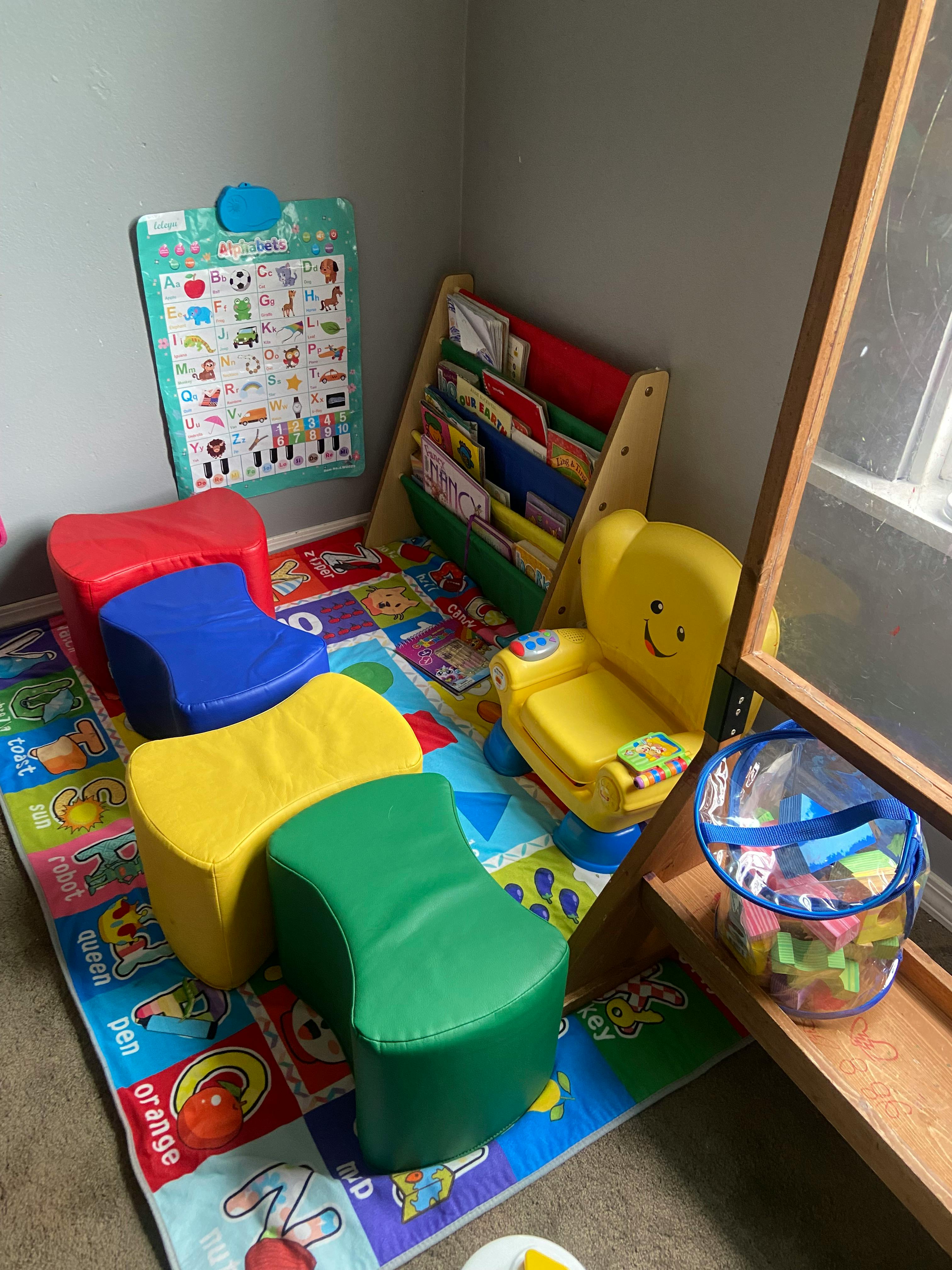 Children's play area with colorful chairs, a book rack, and an alphabet chart