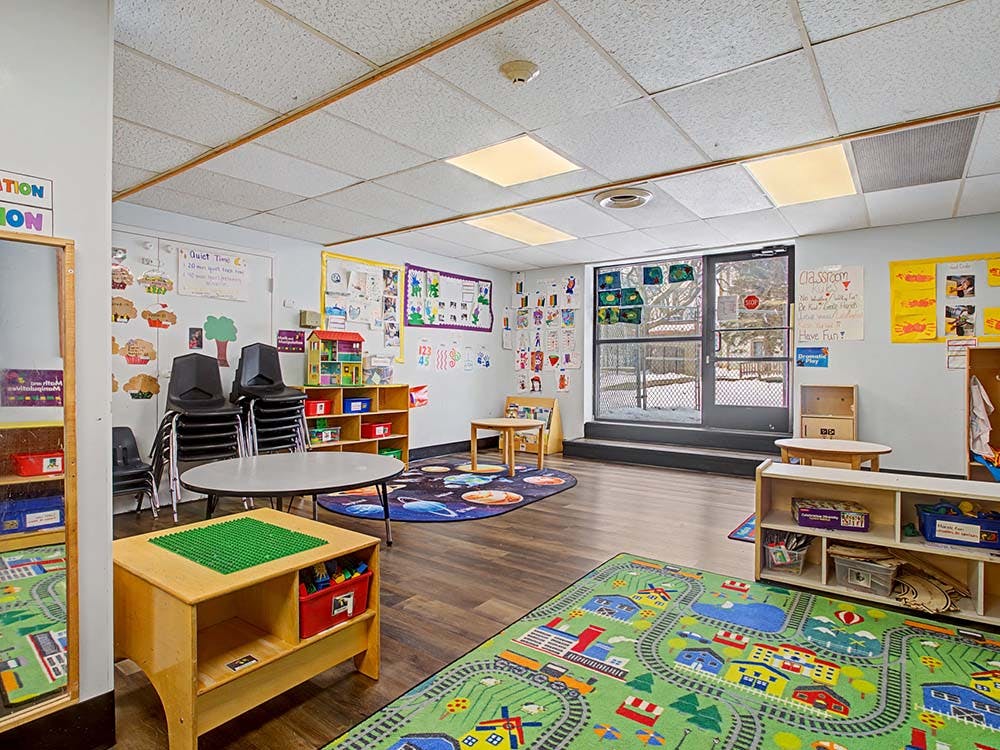 Playroom with small tables, chairs, and play mats on the floor