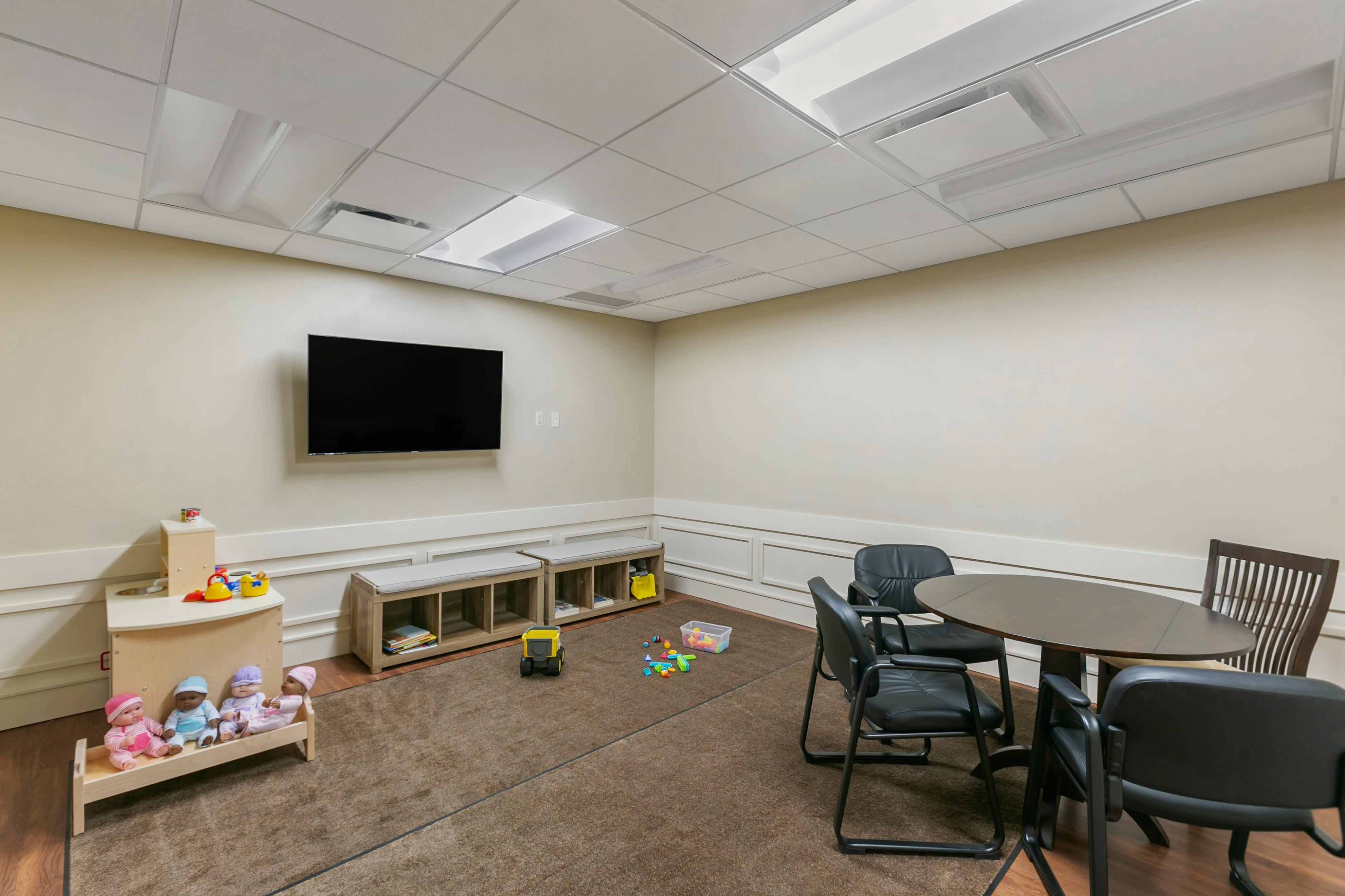 A room with toys, a television, a table with chairs, and benches