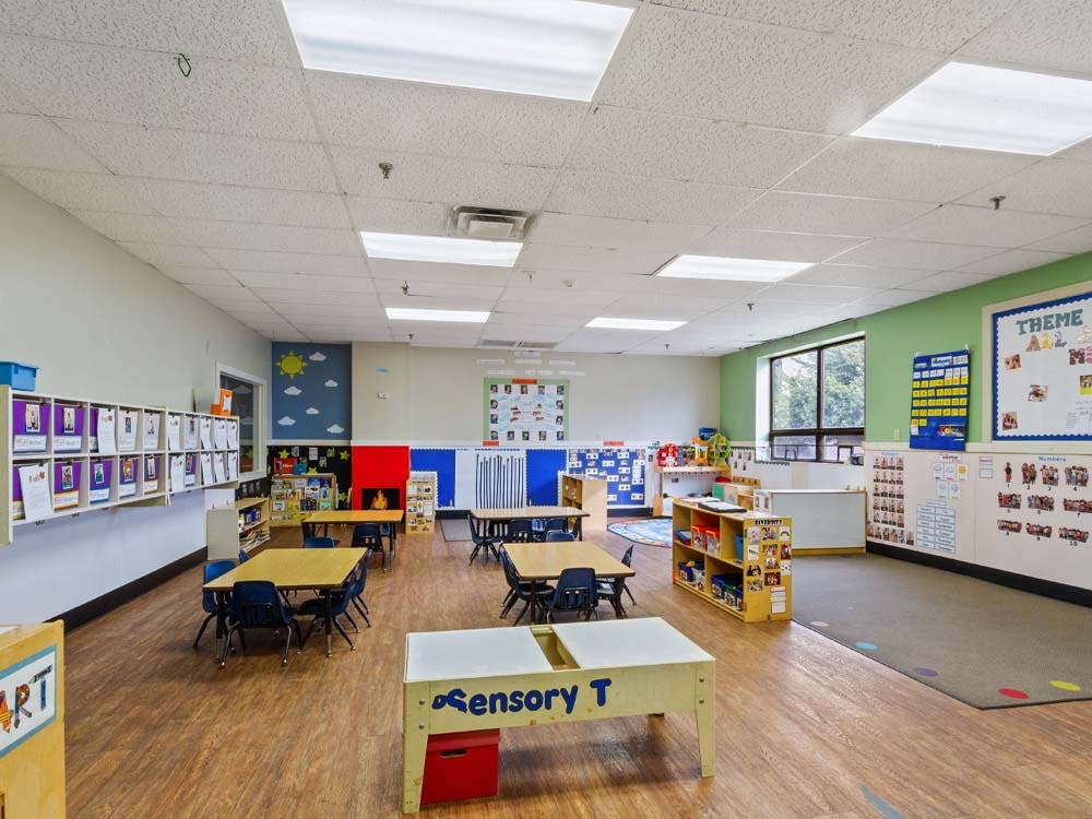 Empty colorful preschool classroom with tables, chairs, and learning materials