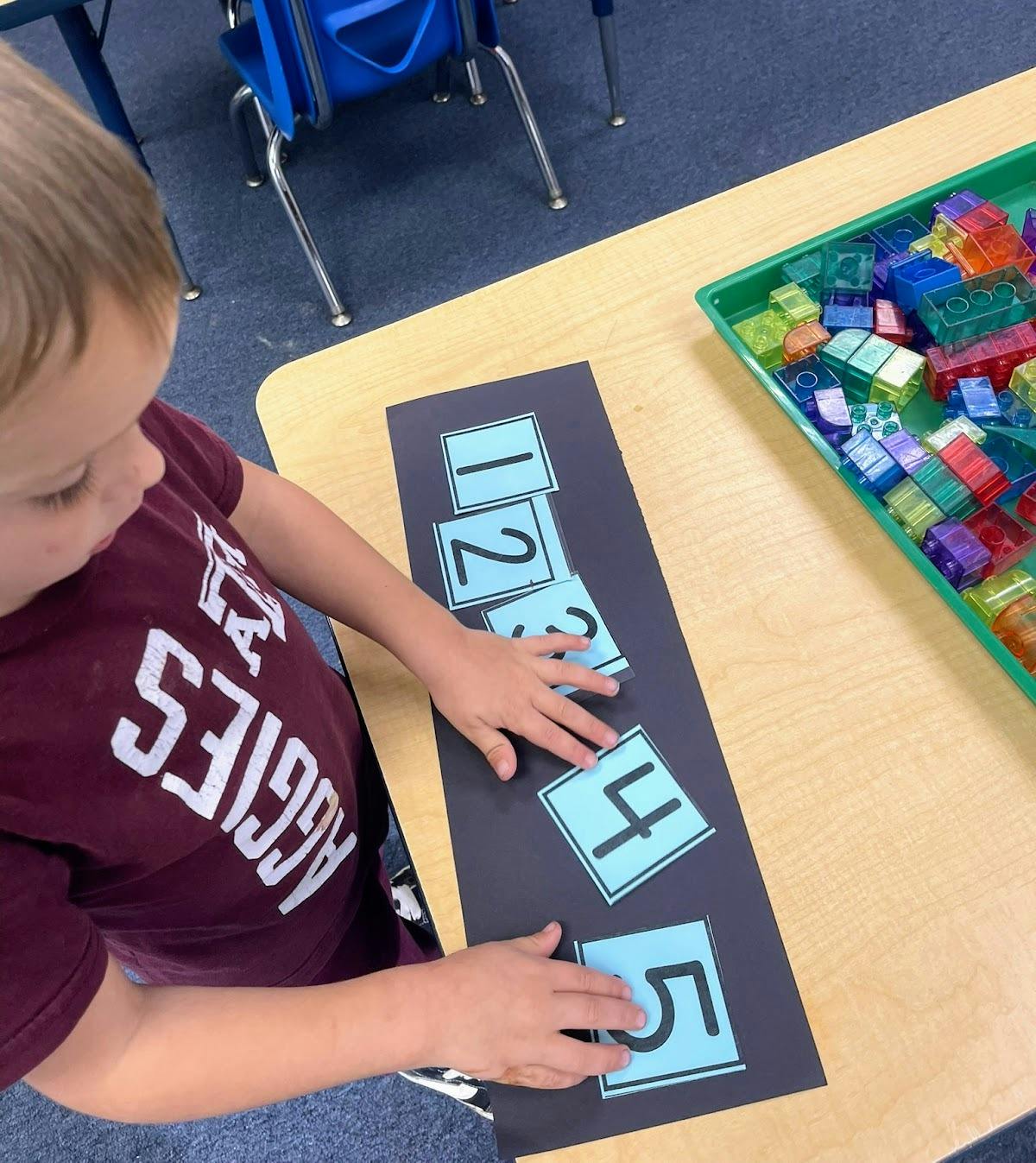 Child arranging number cards one through five on a table