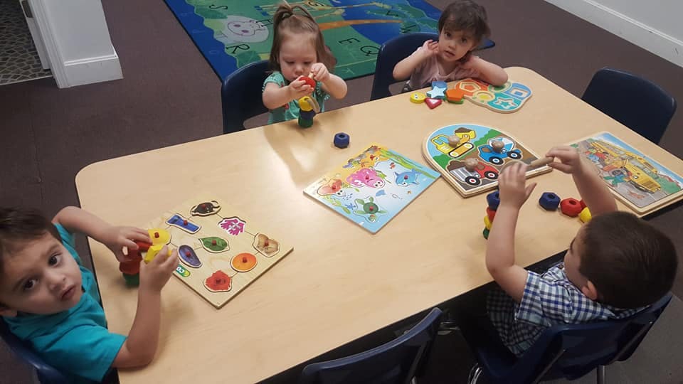 Four children playing with puzzles at a table in a classroom