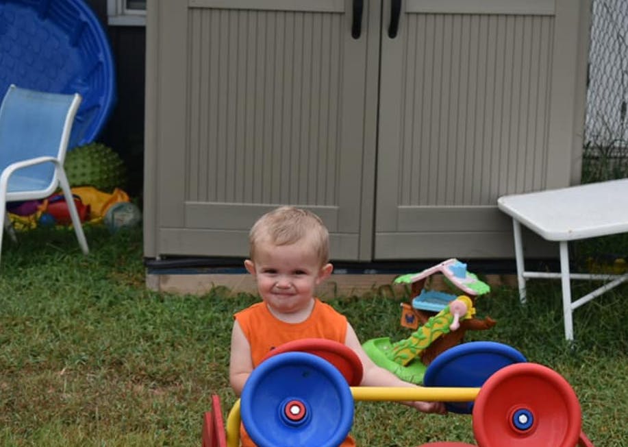 Child in an orange shirt sitting in a toy car