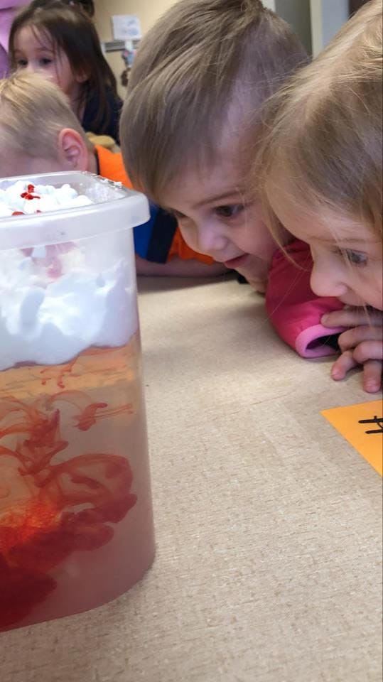 Two children looking at a container with red liquid and white foam