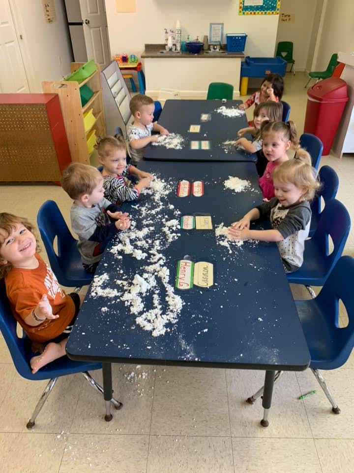 Children playing with flour at tables in a classroom