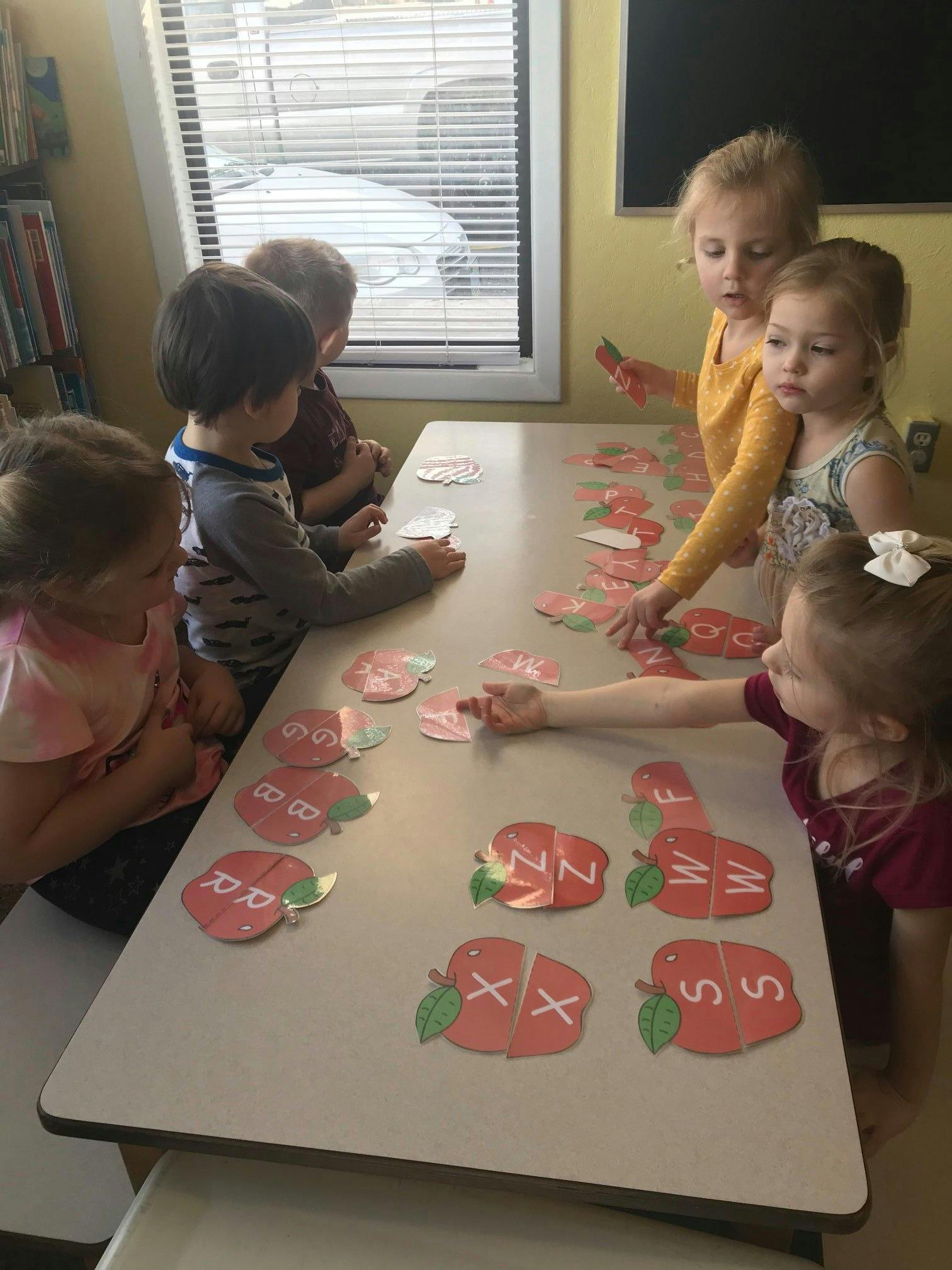 Children playing with apple-shaped letter puzzles at a table
