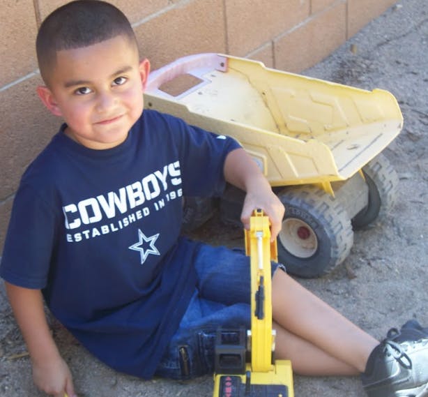 Child sitting on ground with toy construction vehicle and dump truck