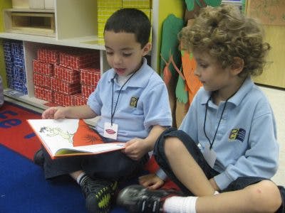 Two children sitting on the floor reading a book in a classroom
