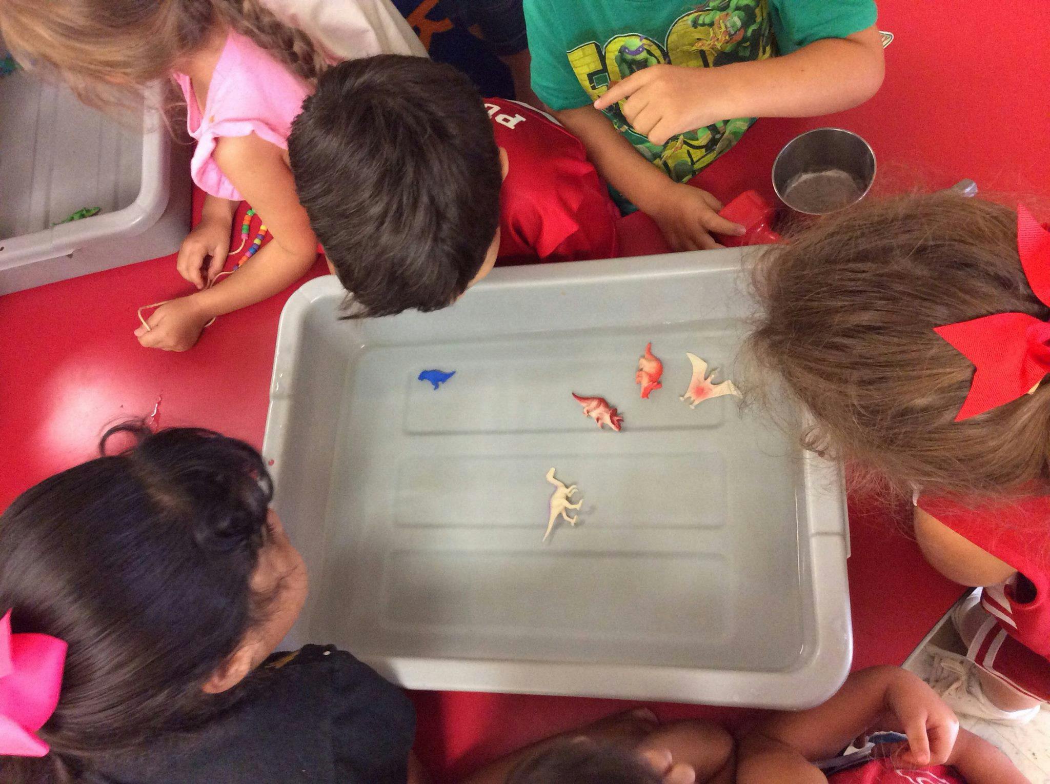 Children gathered around a bin of water with toy dinosaurs