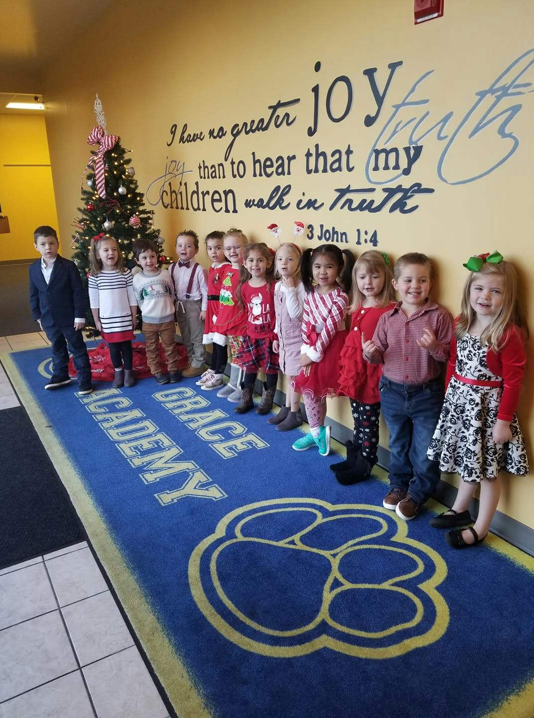 Group of children standing in a line next to a Christmas tree