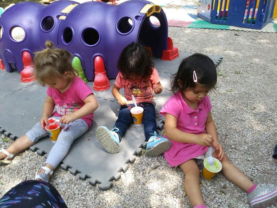 Three children sitting on the ground with cups and spoons