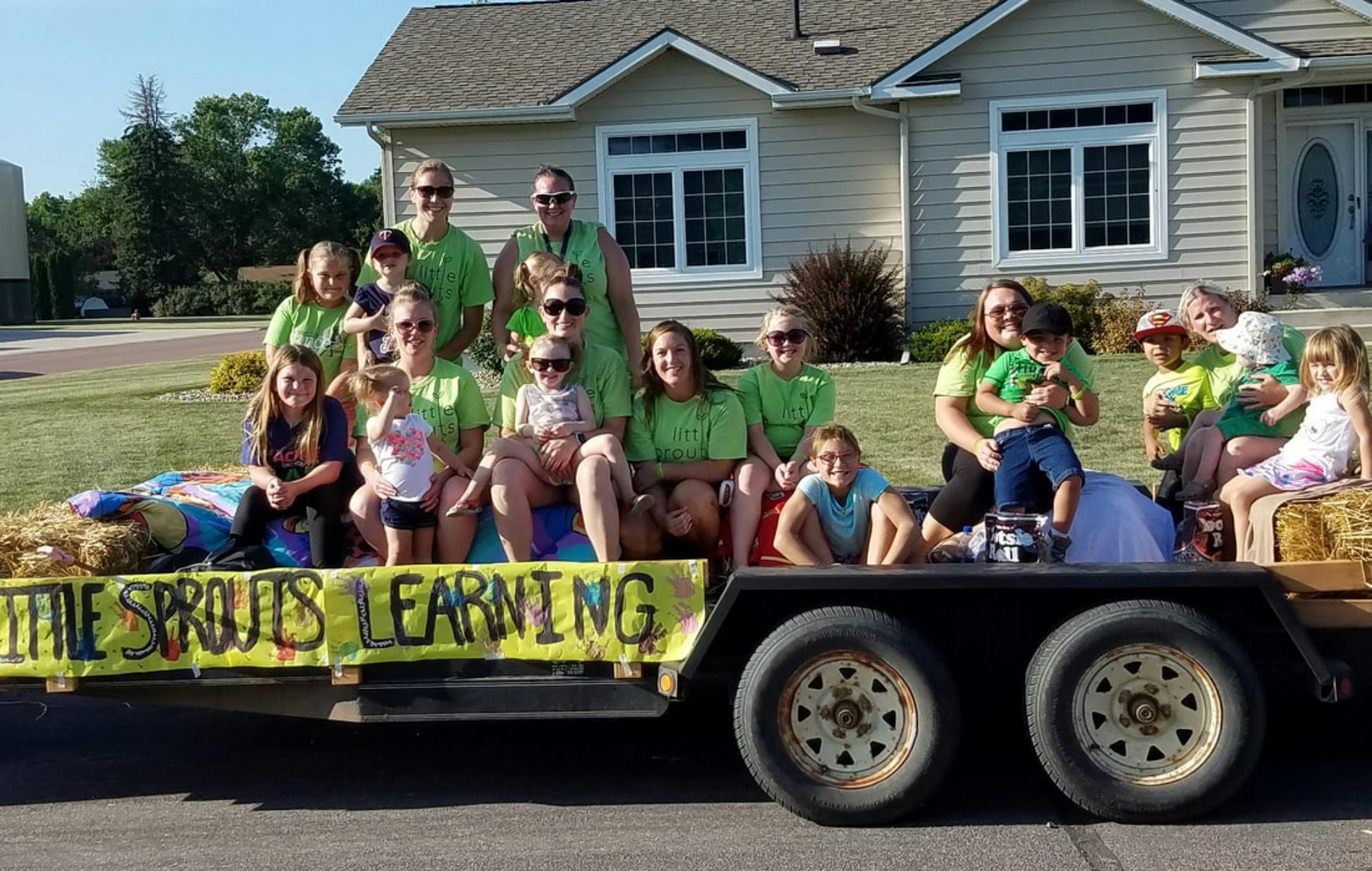 Group of people and children on a trailer with a banner that says "Little Sprouts Learning"