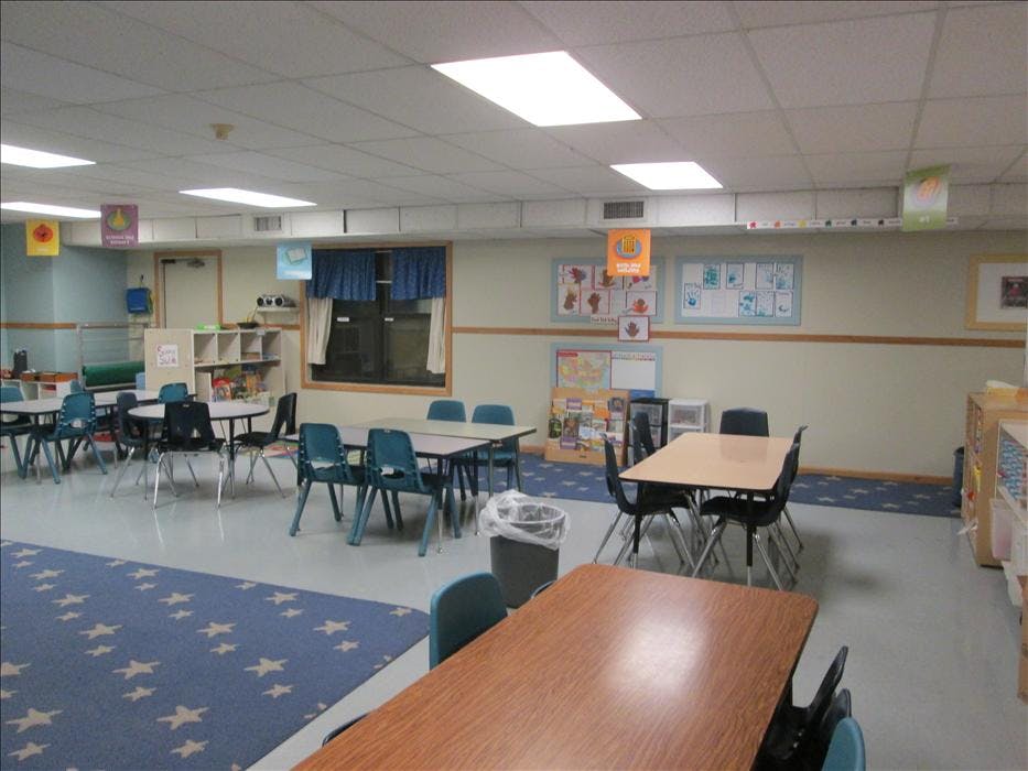 Empty classroom with small tables and chairs, and a blue star-patterned rug