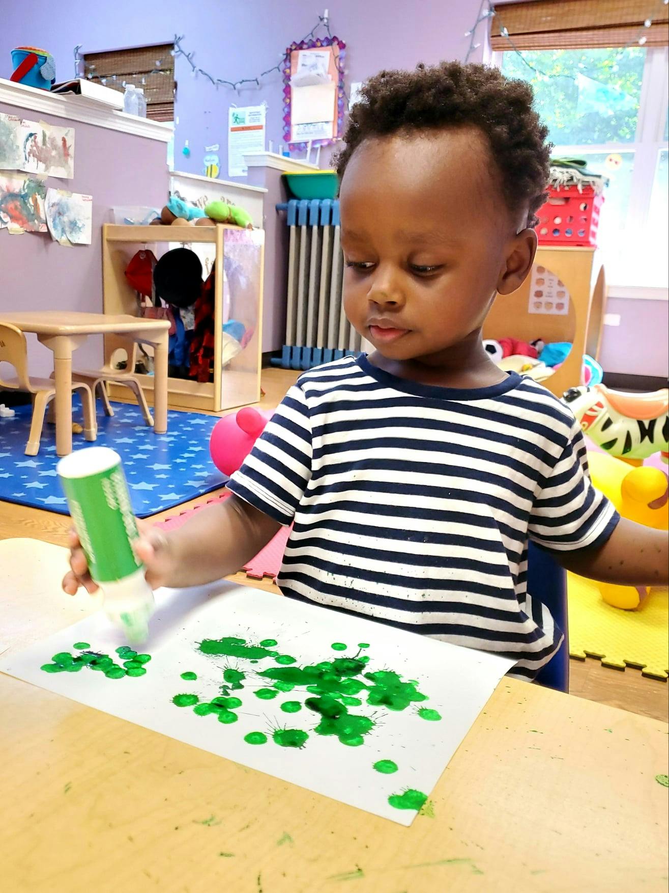 Child using a green paint dauber on paper in a classroom