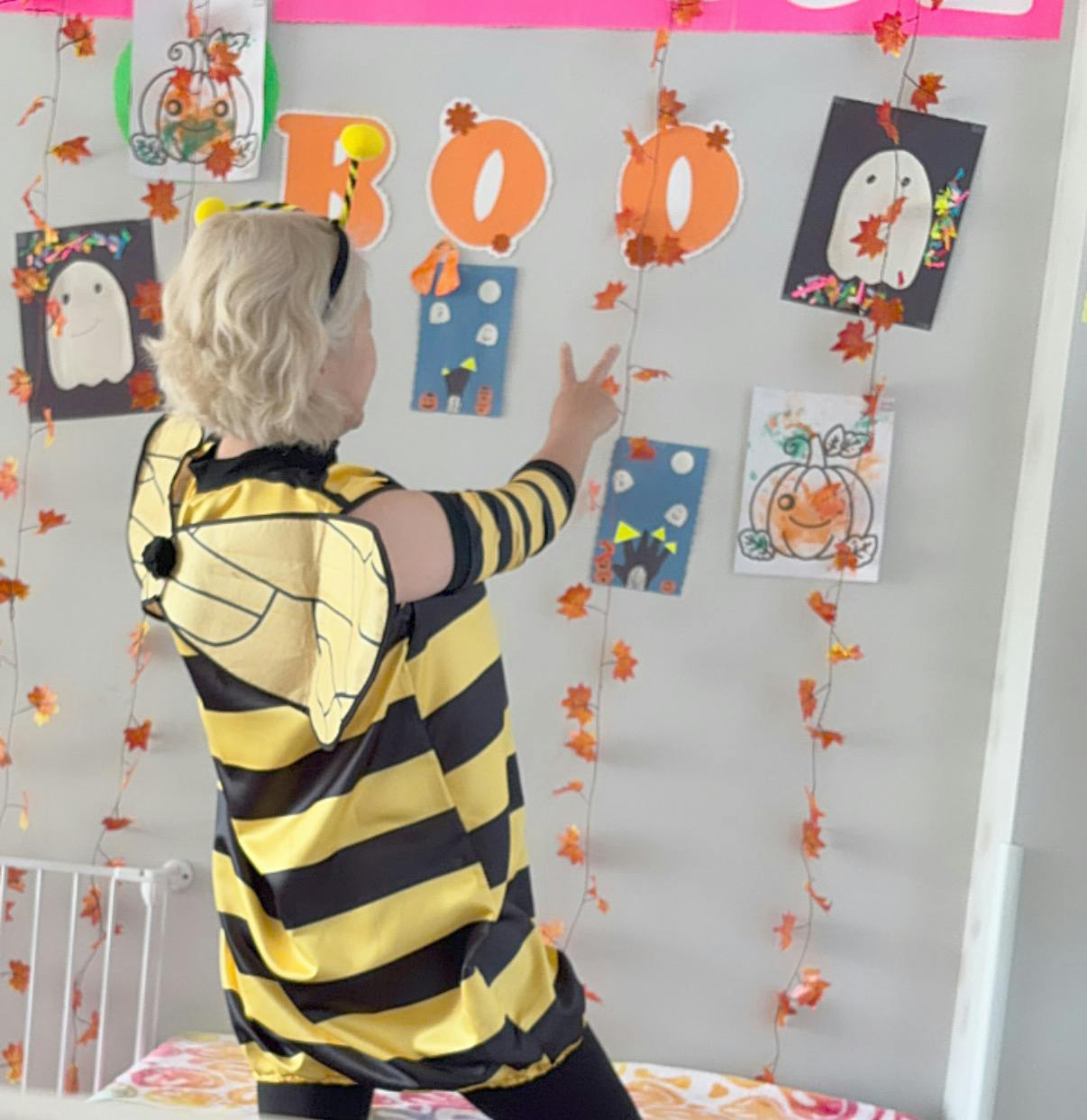 Child in a bee costume pointing at Halloween decorations on a wall