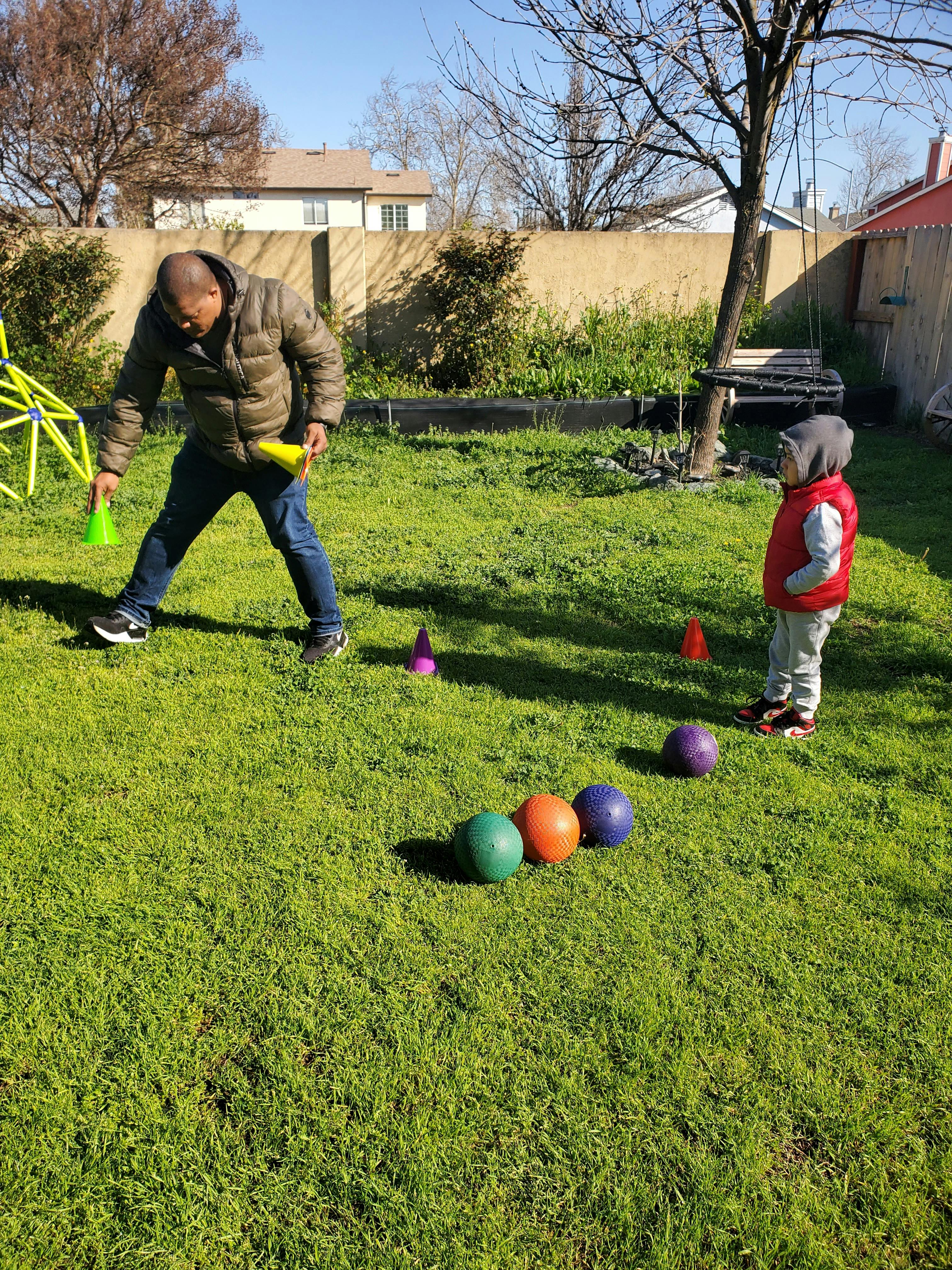Person holding cones and child standing in a grassy yard with balls