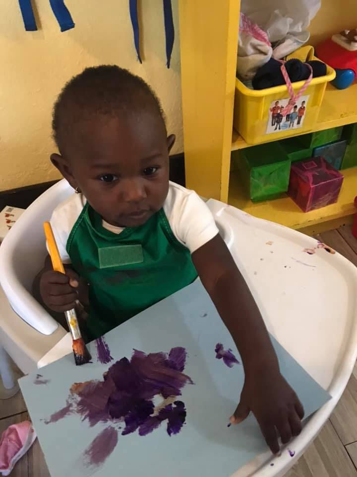 Child in a high chair painting with purple paint on paper