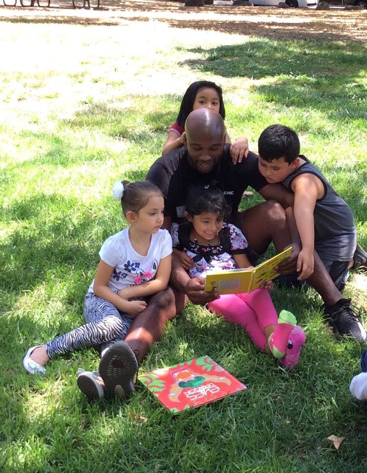Adult person reading a book to three children outdoors