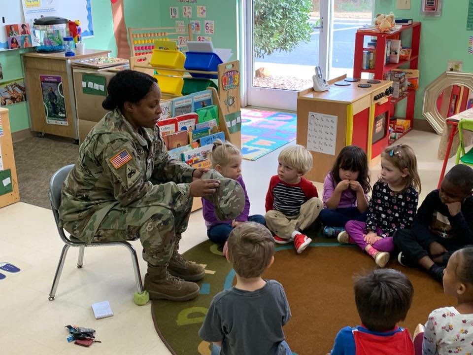 Person in military uniform sitting with children in a classroom