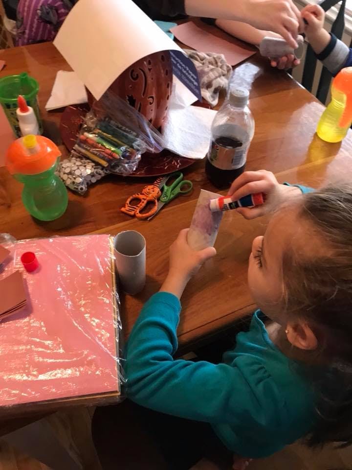 Child gluing paper at a table with craft supplies
