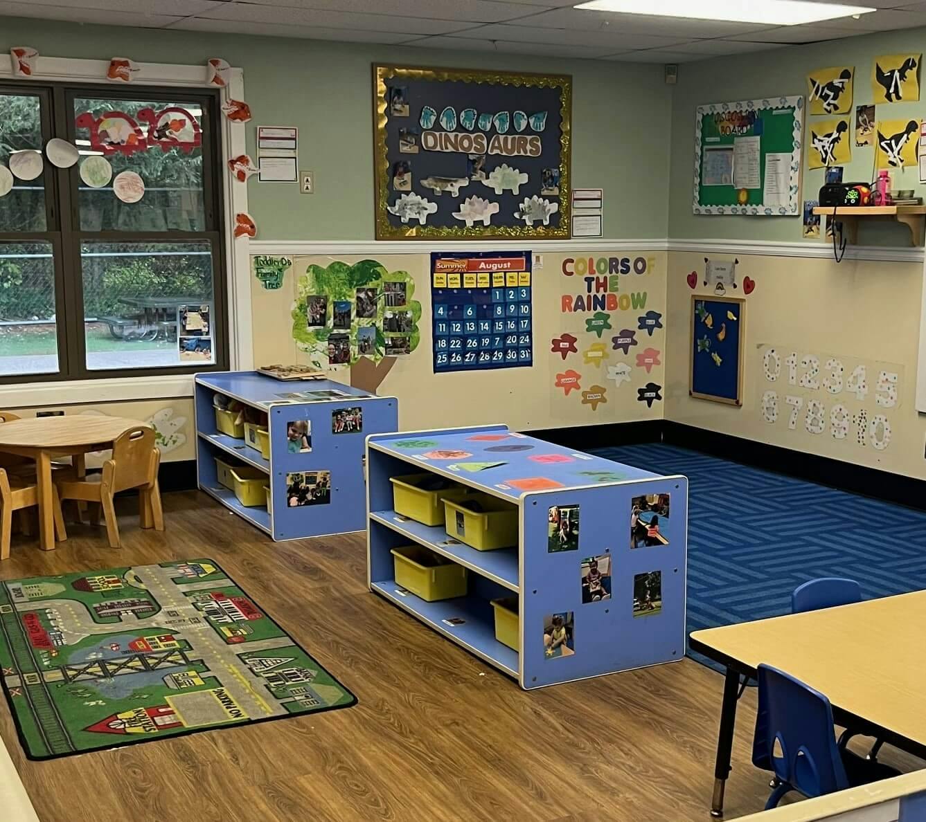 A classroom with small tables and chairs, shelves, and educational posters