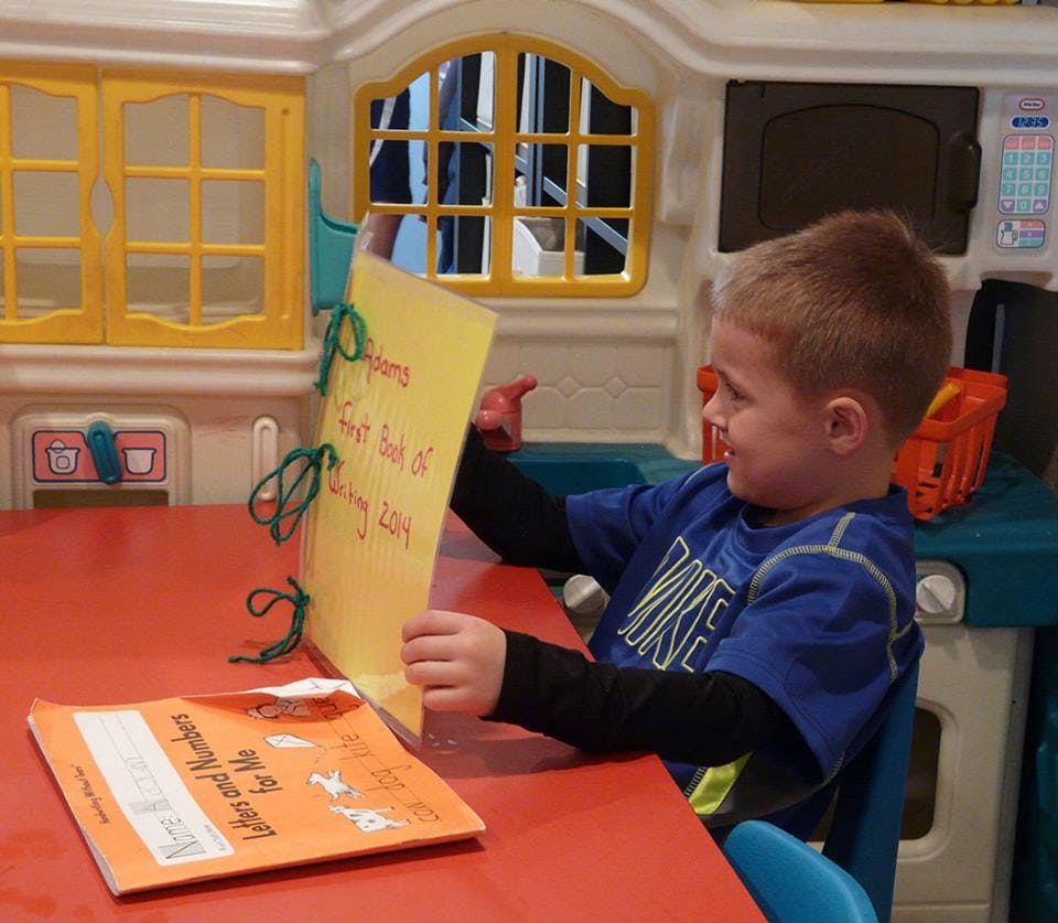 Child sitting at a table, holding up a yellow paper with writing