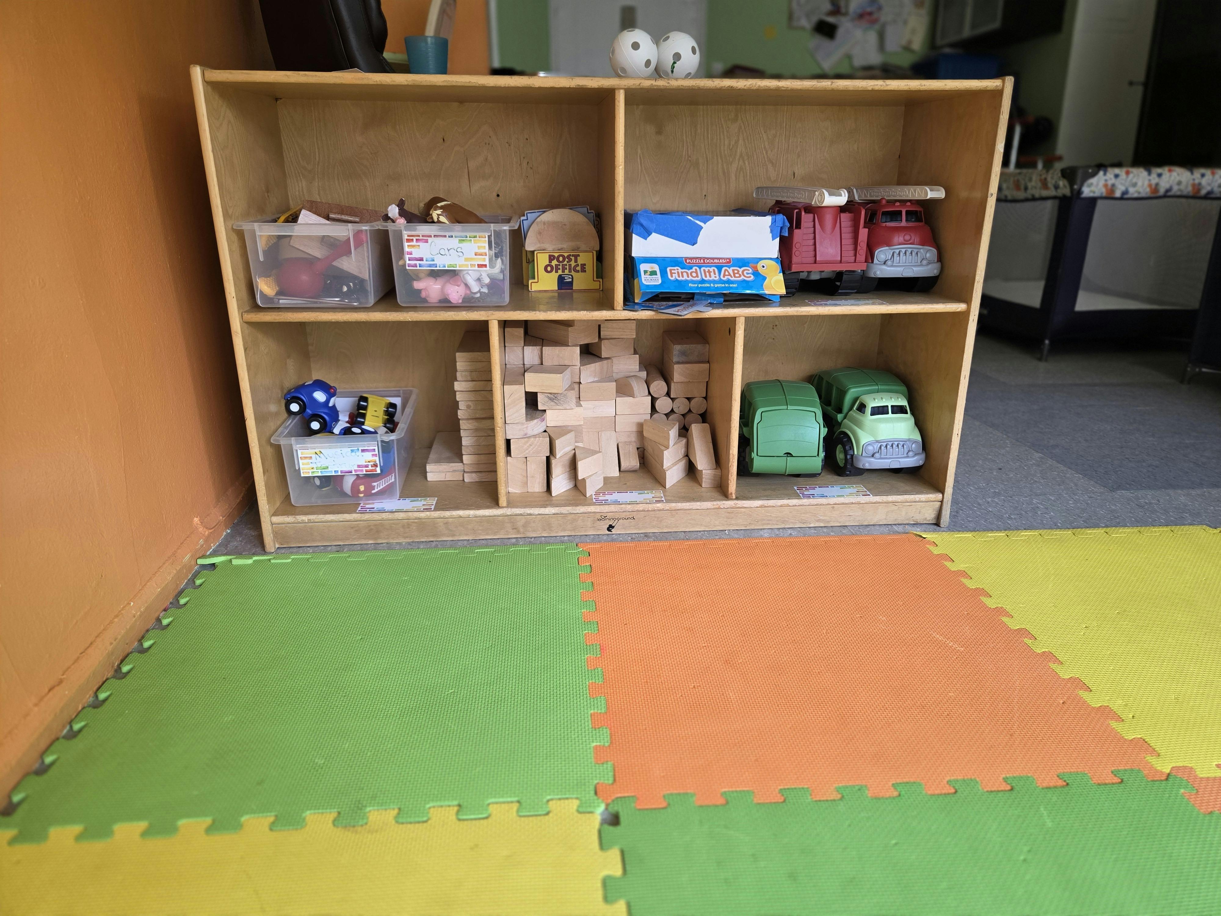 Toy shelf with blocks, toy trucks, and bins of toys in a playroom