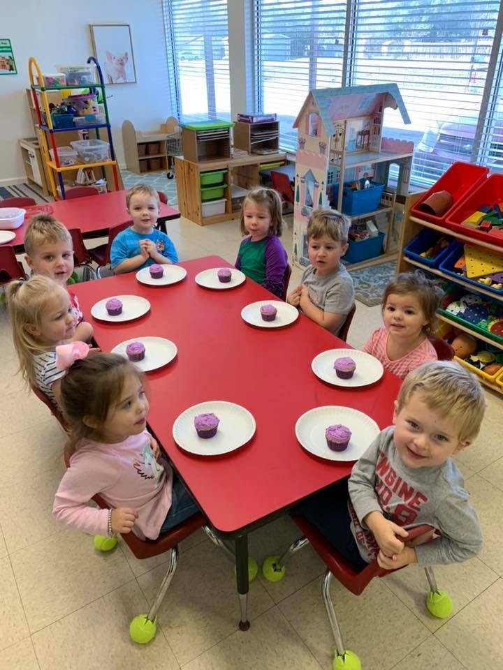 Children sitting at a red table with cupcakes on plates