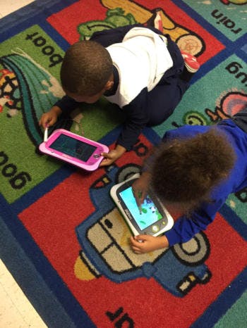 Two children lying on a rug using tablets