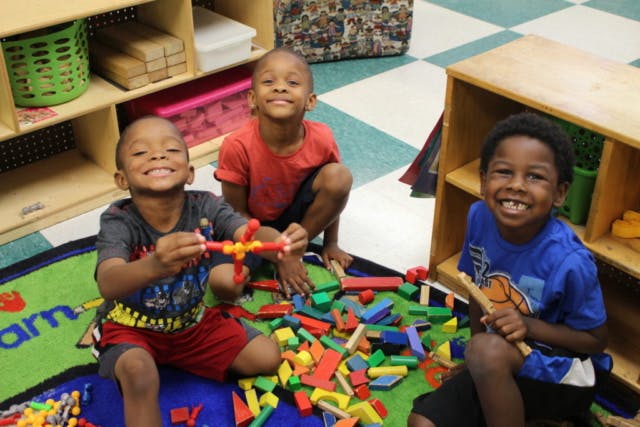 Three children playing with colorful blocks on a rug