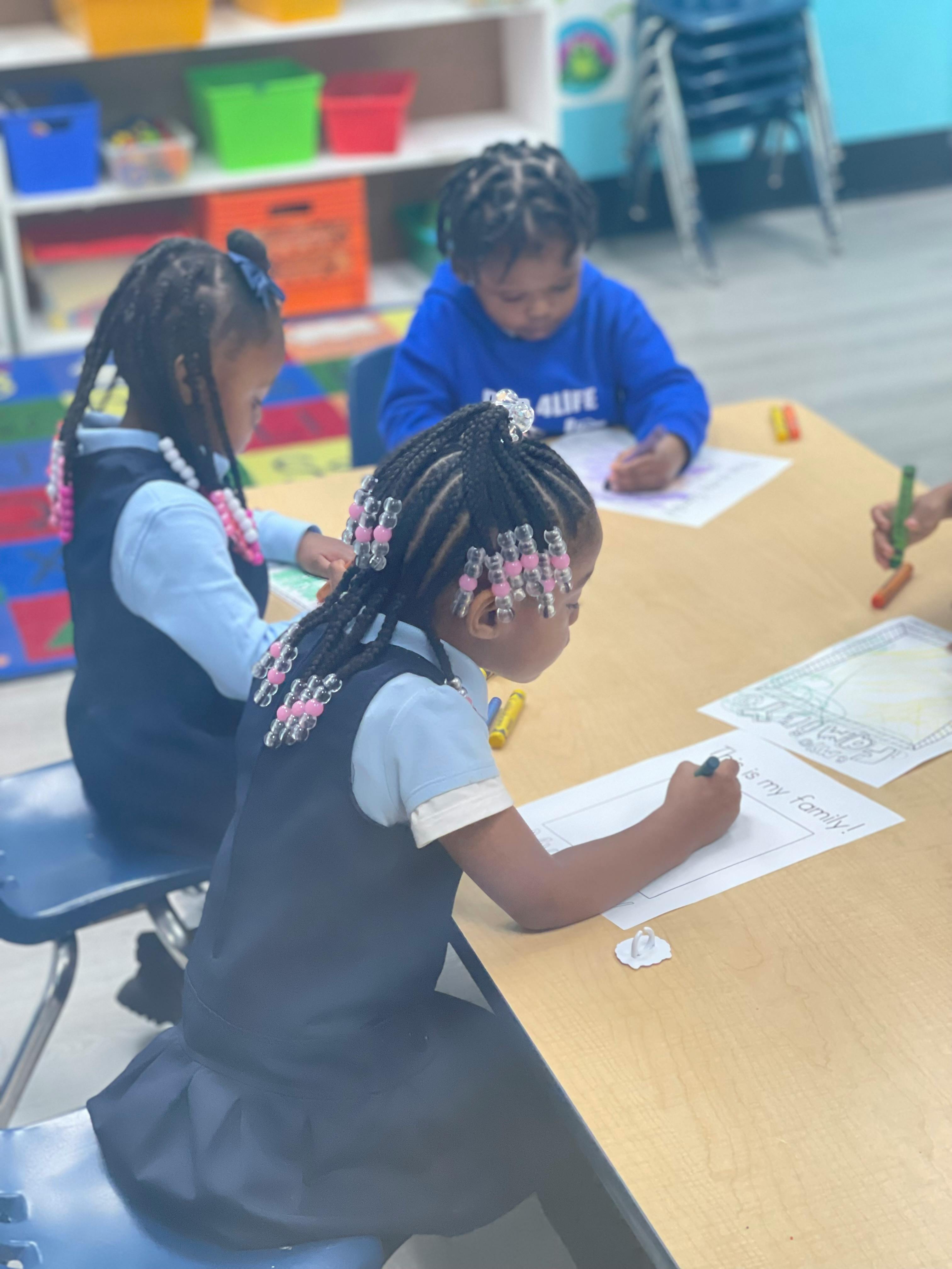 Three children drawing at a table in a classroom