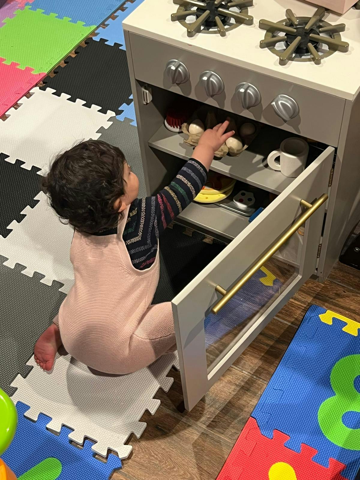 Child reaching into a toy kitchen oven