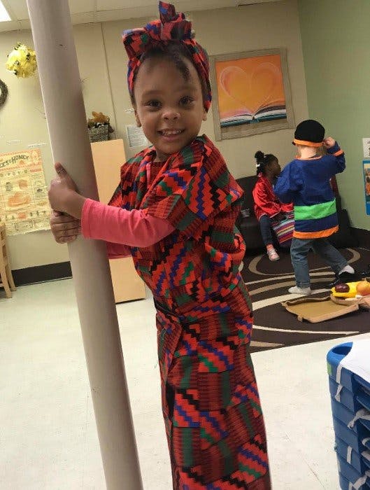 Child in patterned clothing holding a pole in a room