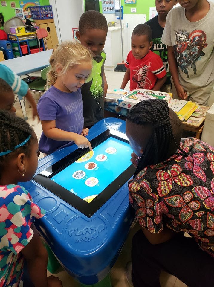 Children and an adult gathered around an interactive digital table